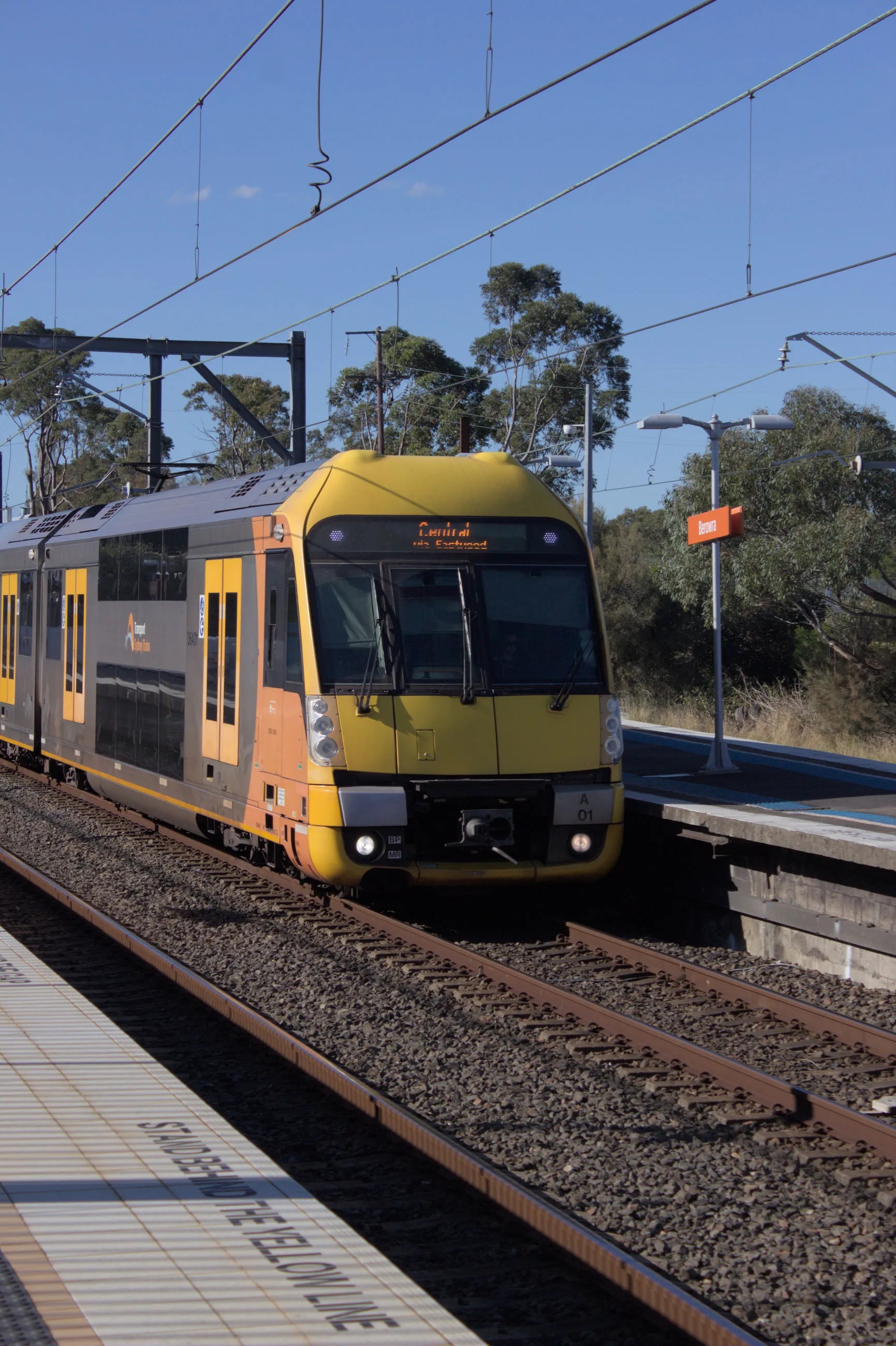 A portrait image of a modern double-decker suburban train with a yellow front and silver body with yellow doors and dark windows at a platform.