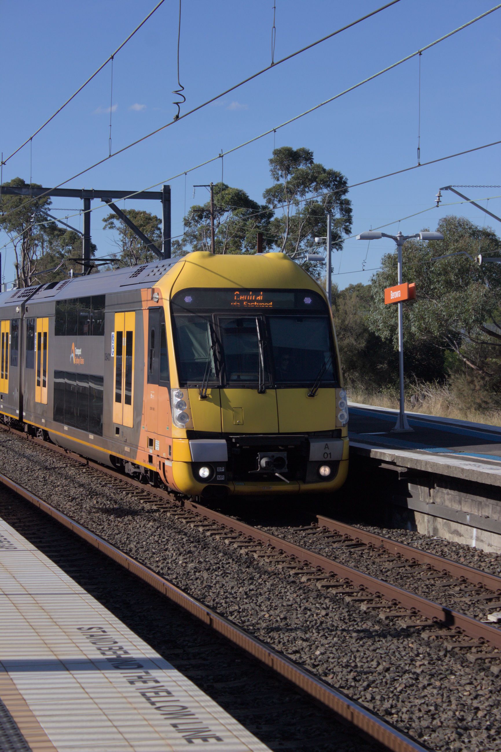 A portrait image of a modern double-decker suburban train with a yellow front and silver body with yellow doors and dark windows at a platform.