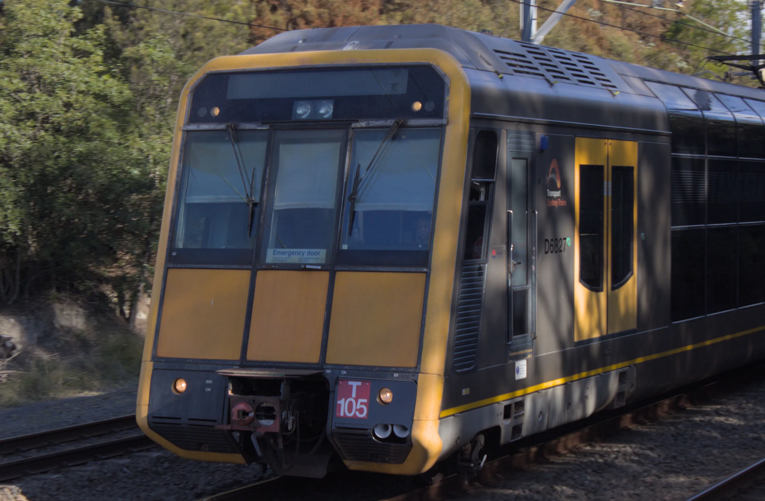 A silver-bodied double-decker suburban train with a flat slanted front moving away from the camera.