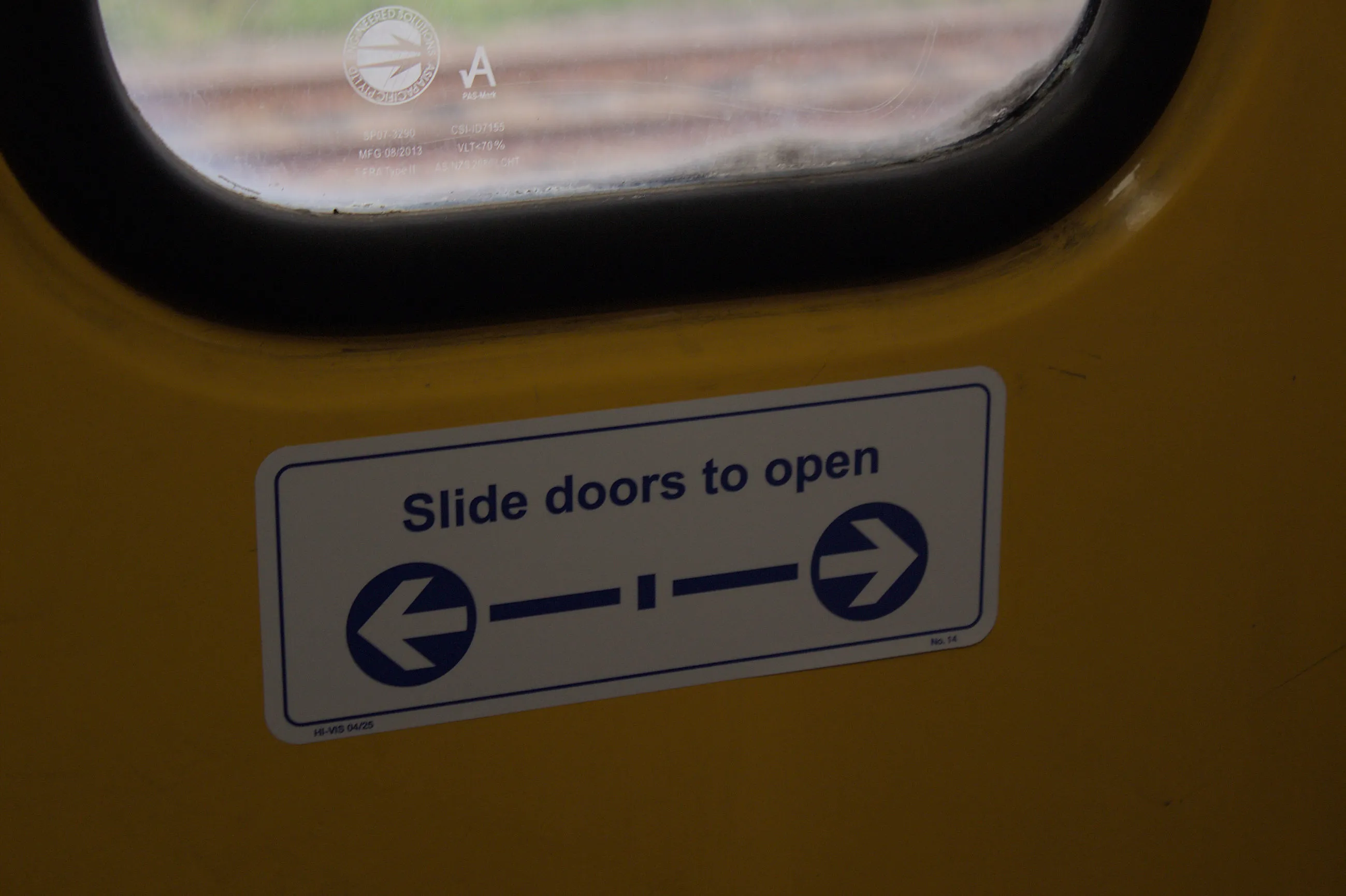 A close up of a white sticker with blue text reading "Slide doors to open" on a yellow door below a window. A related graphic with arrows and lines is below  the text on the sticker. The sticker is in good condition. 